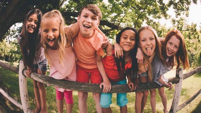 A group of happy children standing on a fence rain and leaning in towards the camera