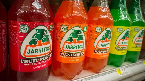 Bottles of various flavors of Jarritos carbonated sodas on a grocery store shelf.