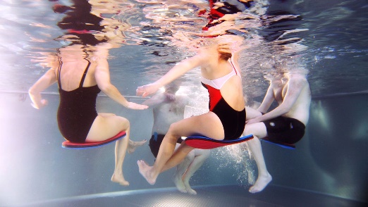 An underwater shot of people sitting on kickboards during a water aerobics class