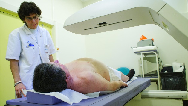 A photo of a female physician and her overweight male patient who is being scanned by a DXA densitometer