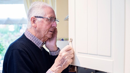  A photo of a confused looking senior man who is looking into a kitchen cabinet.