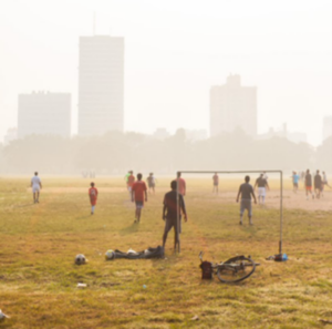 Des gens jouent au soccer en plein air sur un terrain alors que la qualité de l'air est mauvaise et que le smog est visible.