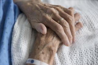 Gros plan sur les mains d'une aînée dans un lit d'hôpital.